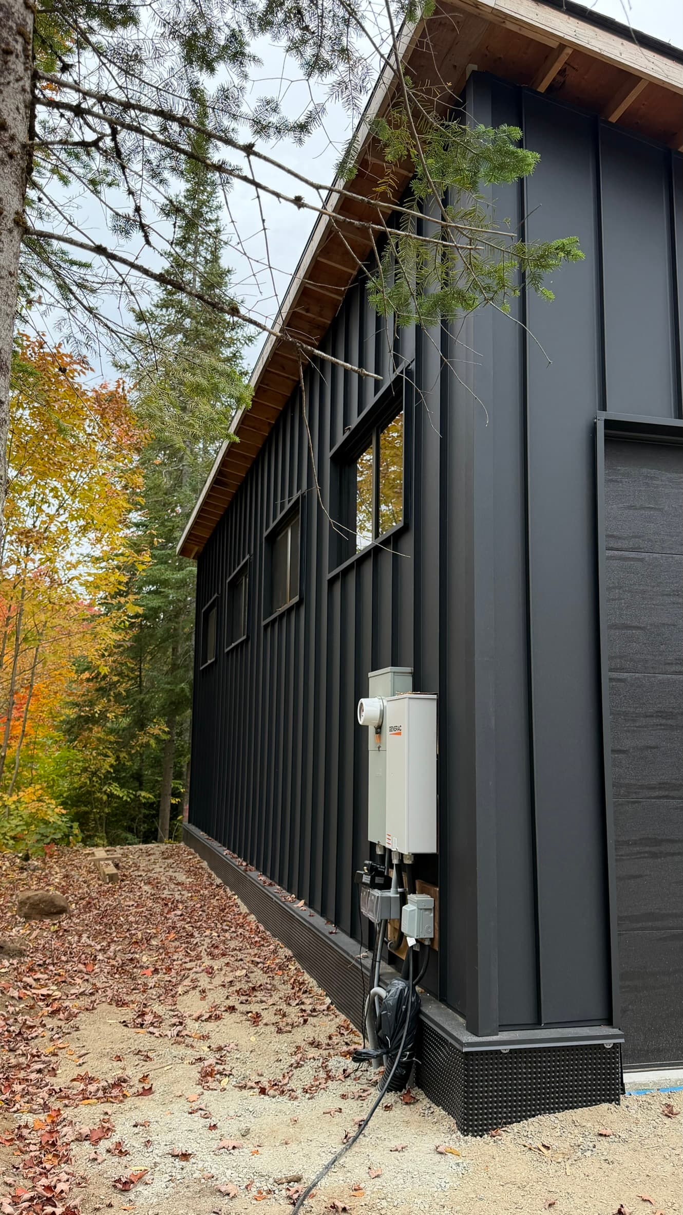 Black vertical metal siding on a two-storey home surrounded by autumn forest — VAH Construction